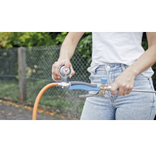 Osoba strieka čistiaci prostriedok na regulátor prúdu vody pripojený k záhradnej hadici.