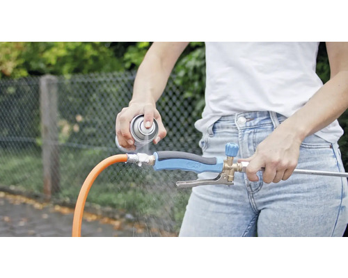 Osoba strieka čistiaci prostriedok na regulátor prúdu vody pripojený k záhradnej hadici.