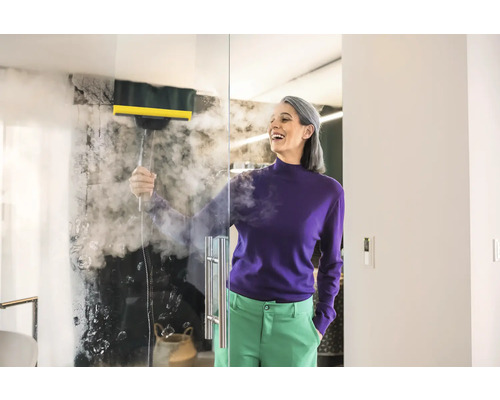 Žena čistí sklenenú stenu parným čističom v kúpeľni
