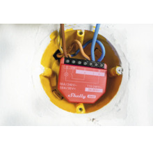 Detailný záber relé Shelly Gen3 v žltej zapustenej krabici s elektrickými vodičmi.