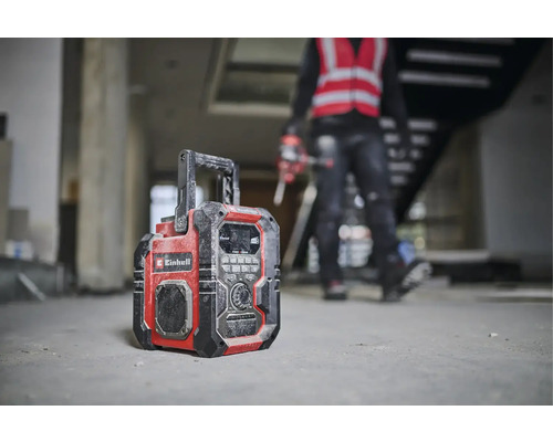 Stavebné rádio značky Einhell stojí na podlahe hrubej stavby.