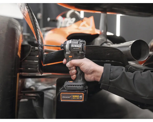 Ruka drží akumulátorový rázový uťahovák DeWalt pred pretekárskym autom