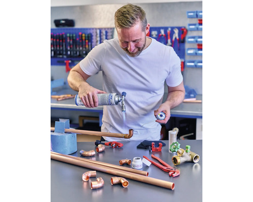 Muž spájkuje medené rúrky plynovým horákom a náradím na stole.