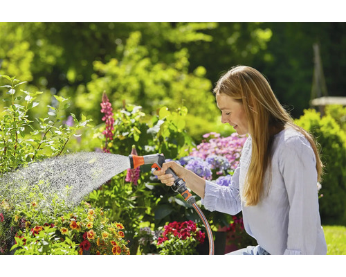 Žena zalieva rastliny záhradnou hadicou v záhrade