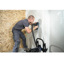 Muž brúsi stenu pomocou brúsky a vysávača