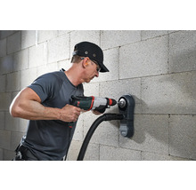 Muž vŕta do steny vŕtačkou a odsávaním prachu.