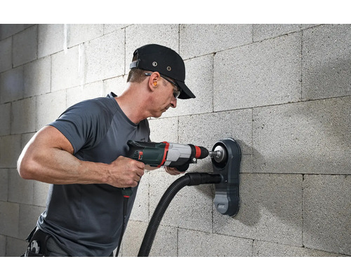 Muž vŕta do steny vŕtačkou a odsávaním prachu.