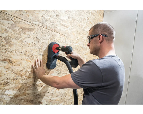 Remeselník vŕta vŕtačkou cez drevenú dosku s odsávaním prachu