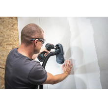 Muž vŕta dieru do steny s nástavcom na vysávač