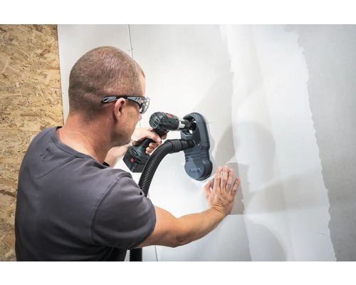 Muž vŕta dieru do steny s nástavcom na vysávač