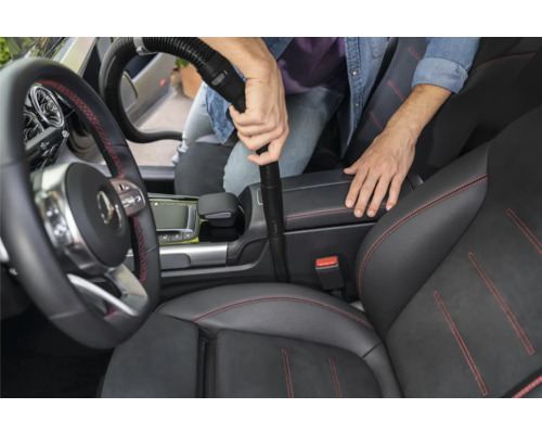 Osoba vysáva interiér automobilu pomocou vysávača