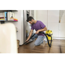 Muž vysáva podlahu v modernom dome žltým viacúčelovým vysávačom.