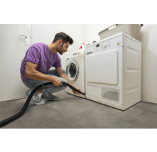 Muž čistí sušičku vysávačom vo svetlej práčovni.