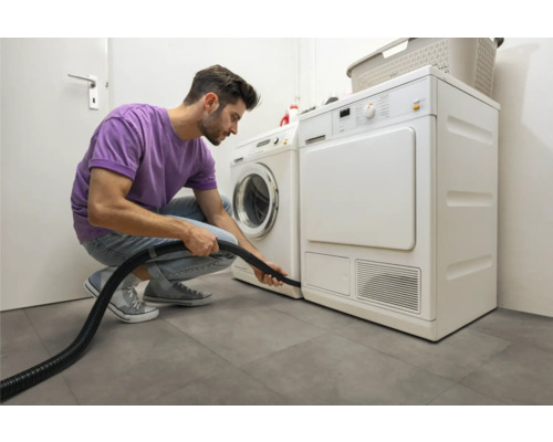 Muž čistí sušičku vysávačom vo svetlej práčovni.