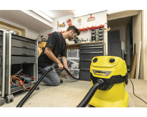 Muž používa žltý vysávač Kärcher v dielni na čistenie podlahy.