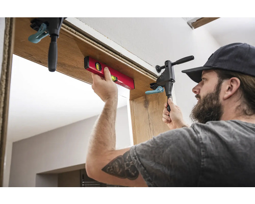 Remeselník montuje zárubňu pomocou vodováhy a skrutkovej svorky.