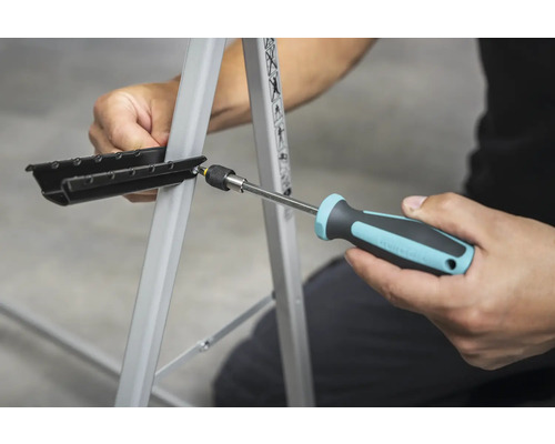 Osoba pripevňuje čierny diel k pracovnému stolu pomocou skrutkovača.