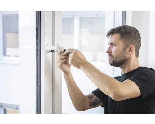 Muž opravuje okennú kľučku pomocou skrutkovača.