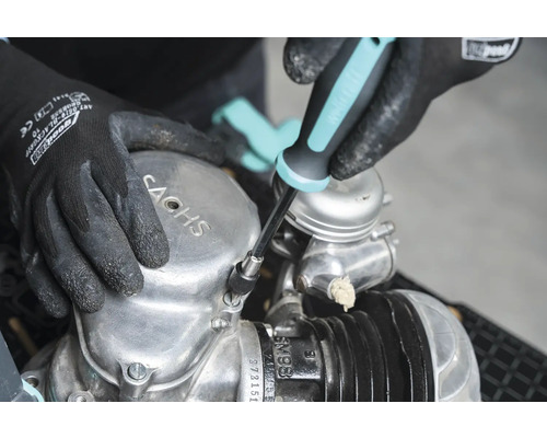 Osoba opravuje motor Sachs pomocou skrutkovača.