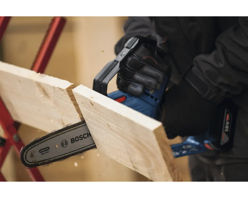 Akumulátorová reťazová píla reže drevenú dosku. Logo spoločnosti Bosch.