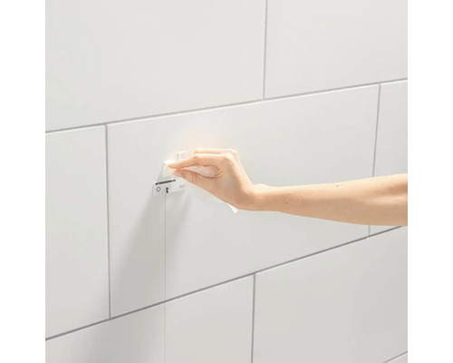 Ruka utiera ovládací panel Grohe na obloženej stene.