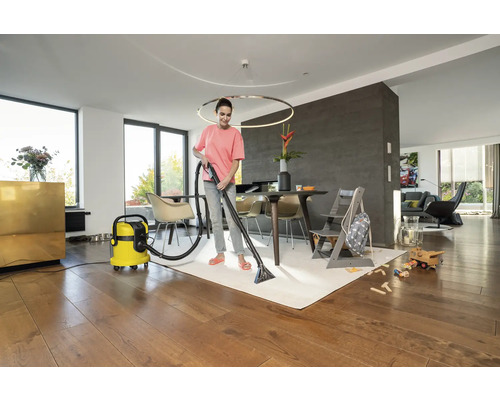 Žena čistí koberec pomocou čistiaceho vysávača v obývacej izbe