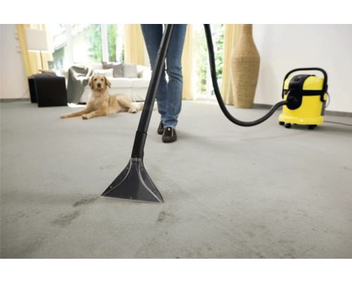 Osoba čistí koberec čistiacim vysávačom v jasnom obytnom prostredí