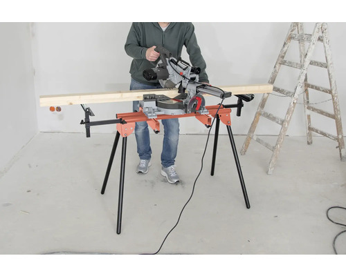 Osoba obsluhuje pokosovú pílu na rezacom stole vedľa rebríka.