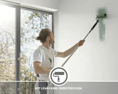 Muž maľuje stenu valčekom a hlinenou farbou.