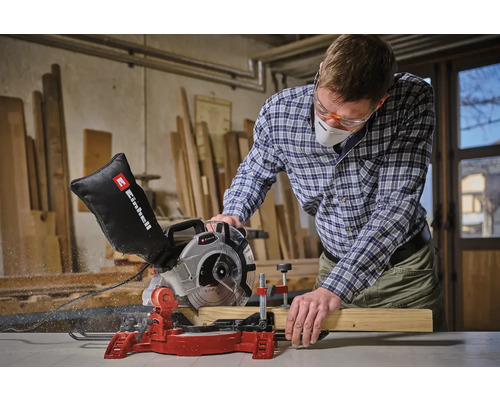Muž s ochrannými okuliarmi a respirátorom reže drevenú dosku pokosovou pílou Einhell.
