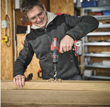 Muž vŕta otvor do drevenej dosky pomocou akumulátorového skrutkovača.