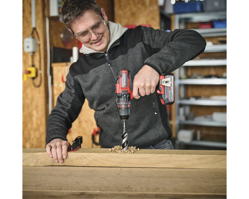 Muž vŕta otvor do drevenej dosky pomocou akumulátorového skrutkovača.