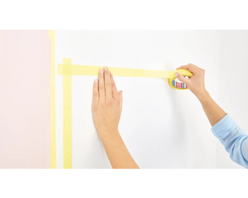 Osoba lepí maliarsku pásku na stenu.
