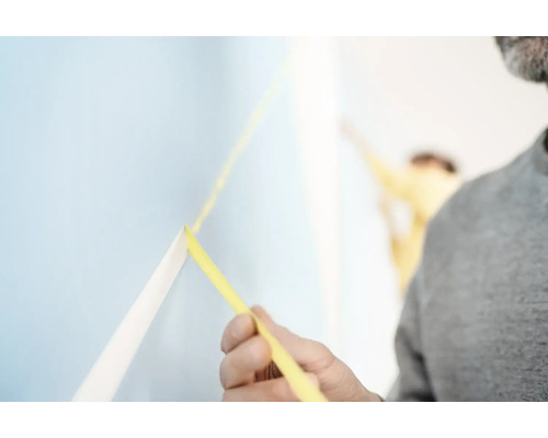 Muž upevňuje maliarsku krepovú pásku na stenu