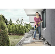 Žena čistí chodníkové dosky vysokotlakovým čističom v záhrade.