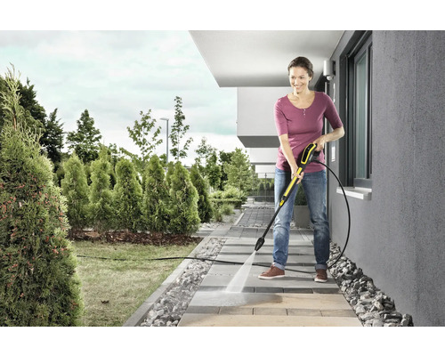 Žena čistí chodníkové dosky vysokotlakovým čističom v záhrade.