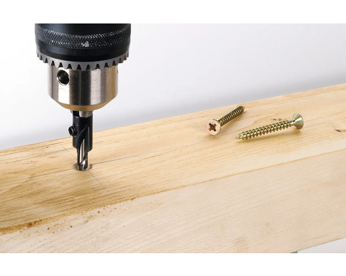Vŕtací stroj so zápustkovým vrtákom vŕta do drevenej dosky, vedľa ležia dve skrutky