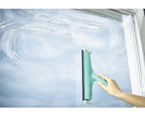 Ruka čistí sklenený povrch stierkou na okná