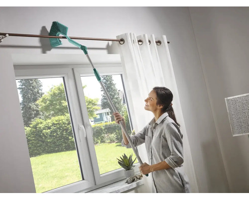 Žena čistí záclonovú tyč teleskopickým prachovkou vo svetlej miestnosti