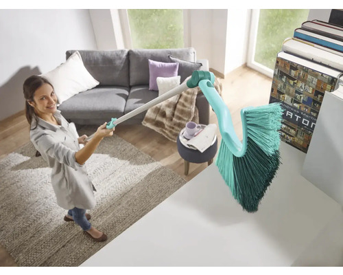 Žena používa kefu s rukoväťou na upratovanie v obývacej izbe.