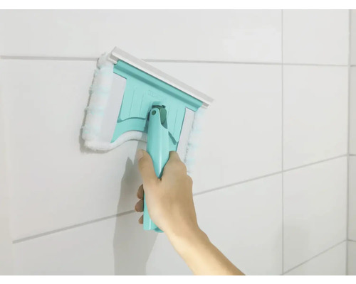 Ruka používa stierku na okná s návlekom z mikrovlákna na obkladanej stene