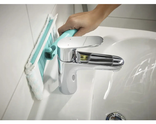 Čistenie steny kúpeľne s kúpeľňovou stierkou vedľa umývadla.