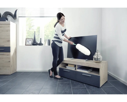 Žena utiera prach z televízora prachovkou v obývacej izbe.