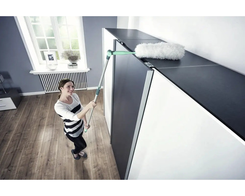 Žena čistí povrch skrine prachovkou.