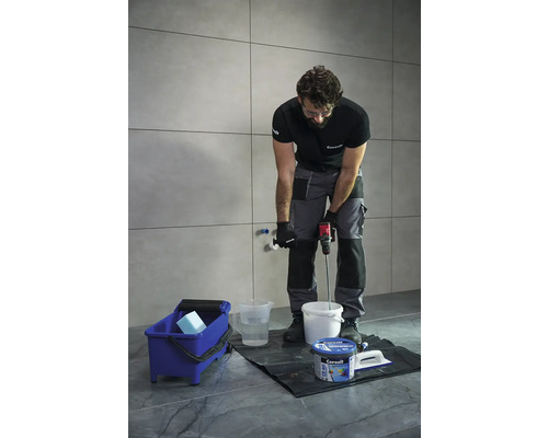 Remeselník mieša lepidlo na obklady miešadlom vo vedre.