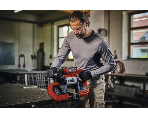 Muž reže kov akumulátorovou pásovou pílou Einhell v dielni