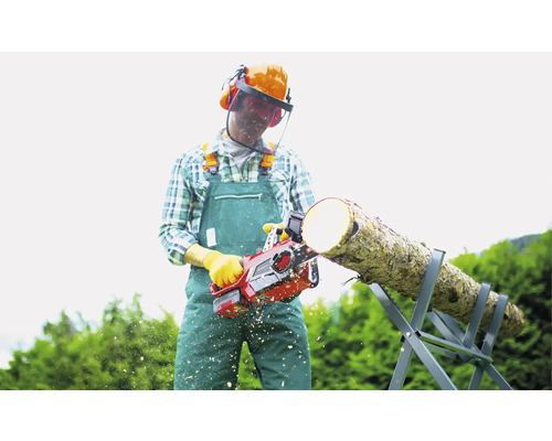 Muž pília drevo motorovou pílou na koze, má na sebe ochranný odev