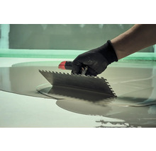 Remeselník rozotiera nivelačnú hmotu stierkou.