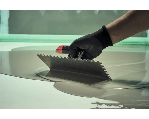 Remeselník rozotiera nivelačnú hmotu stierkou.