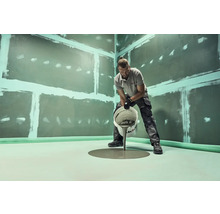 Remeselník leje vyrovnávaciu hmotu do kúpeľne s utesnenými stenami.